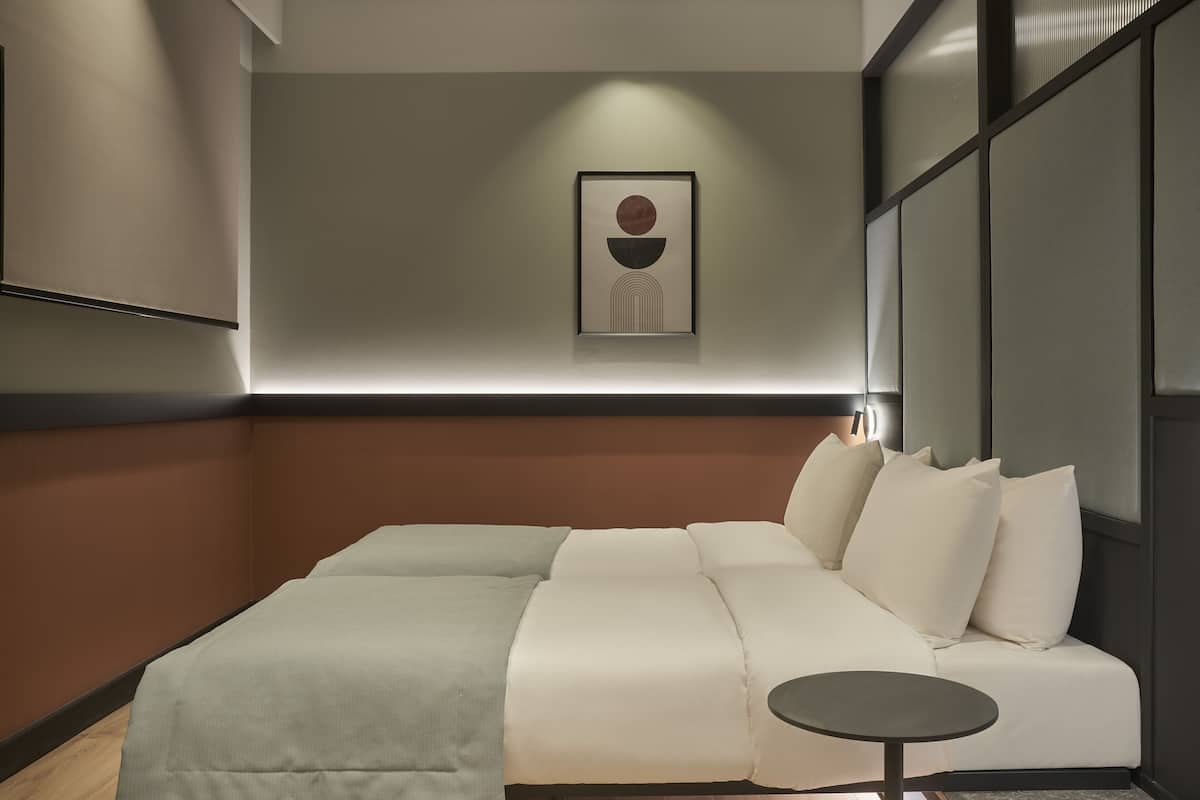 Moderni hotellihuone, jossa on suuri sänky, pieni pyöreä pöytä ja seinällä oleva kehystetty taideteos.