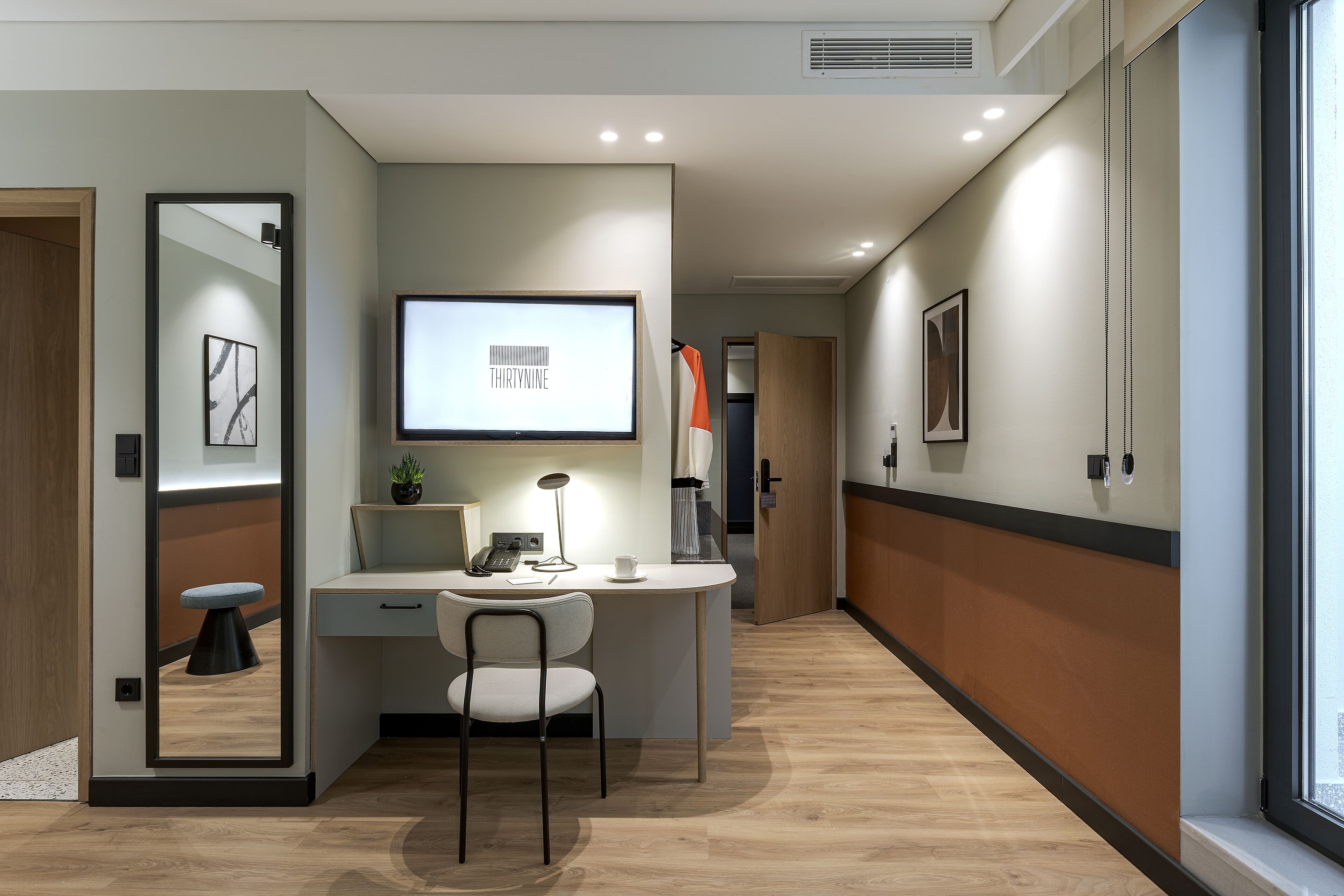 A modern hotel room with a desk, chair, and a large mirror.