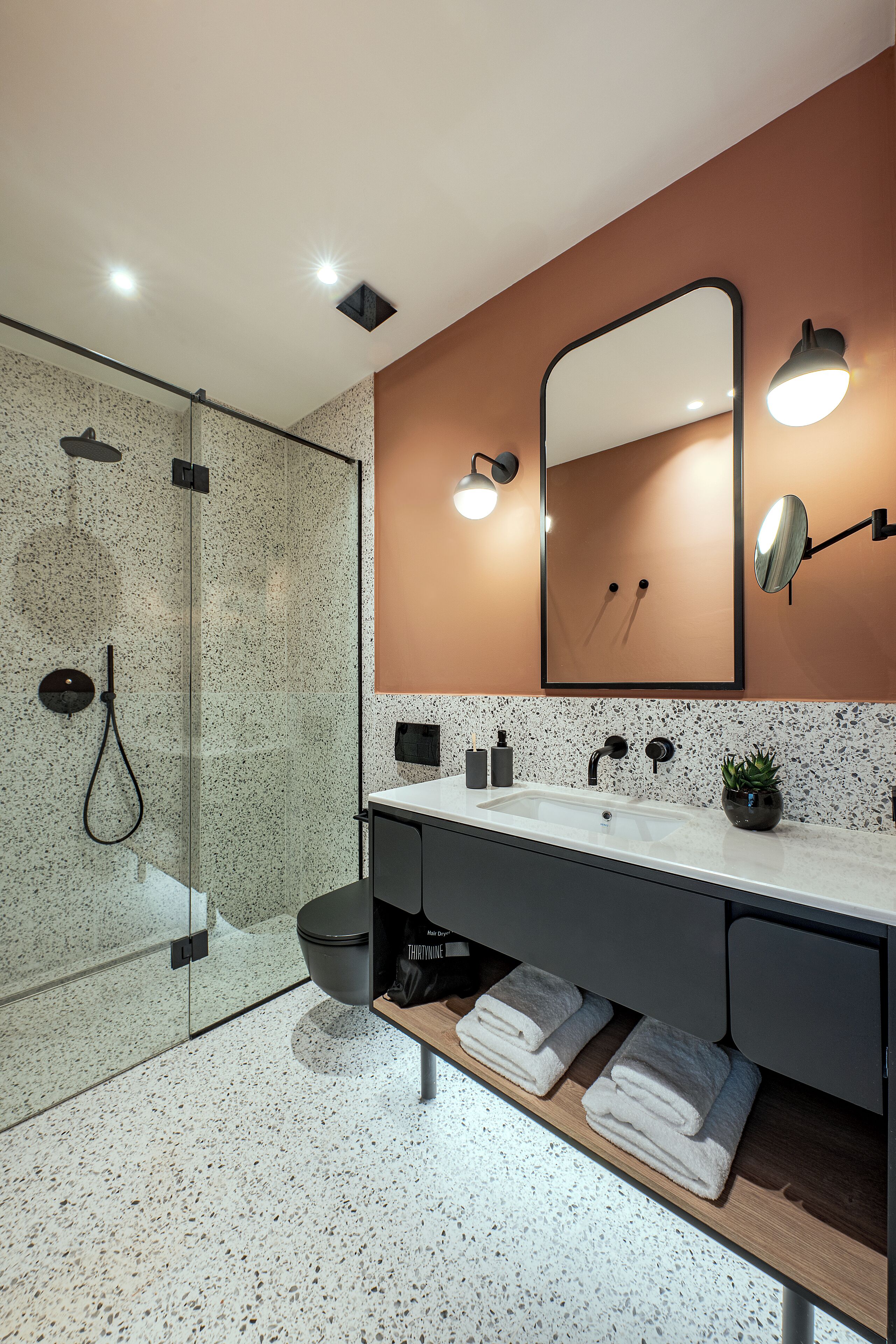 Une salle de bain moderne avec une douche à parois de verre, un lavabo blanc avec un robinet noir et un miroir agrémenté de deux appliques murales.
