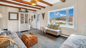 A spacious room with a wooden ceiling, a large window with a view, a sofa, a cabinet, and a wooden crate. - Sea Captains Cottage! (Surry)