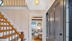 A hallway with a wooden staircase, a dark door, and a cozy seating area with a lamp. - Sea Captains Cottage! (Surry)