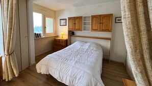 Quarto com cama, cabeceira de madeira, mesa de cabeceira, luminária e janela com cortinas.