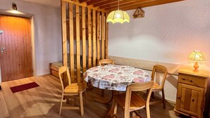 Uma área de refeições acolhedora com uma mesa e cadeiras de madeira, toalha de mesa estampada e um abajur em uma mesinha lateral.