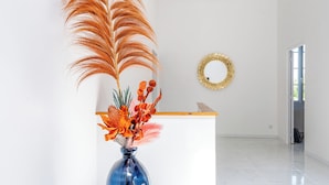 A modern room with a white reception desk, a clear vase with decorative flowers, and a wooden ceiling beam. - La Bastide des Joncquiers (L'Isle-sur-la-Sorgue)