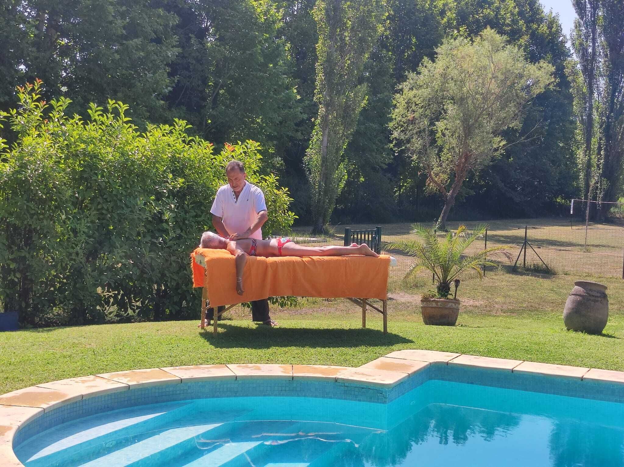 Une personne effectue un massage sur une table à l’extérieur, avec une piscine en arrière-plan.