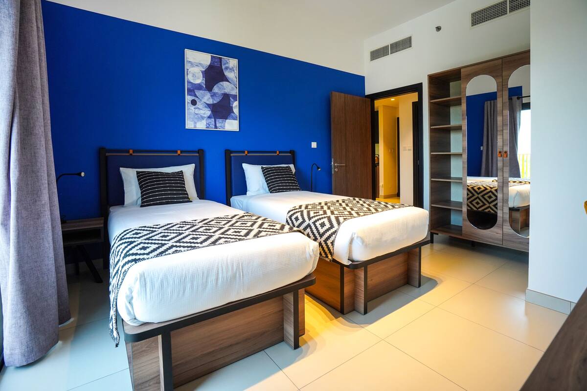 A hotel room with two beds, a wardrobe, and a painting on the wall.