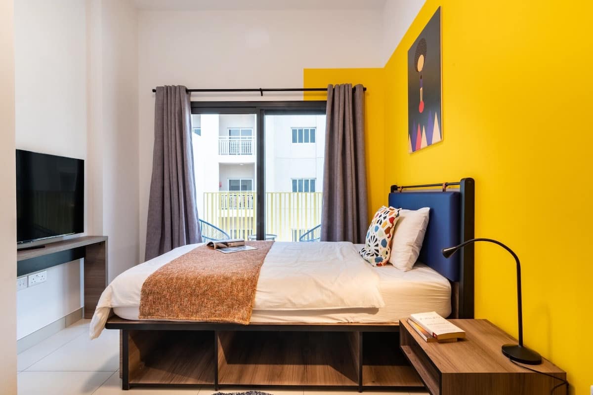 A modern hotel room with a bed, a TV, a bedside table, and a view of the outside balcony.