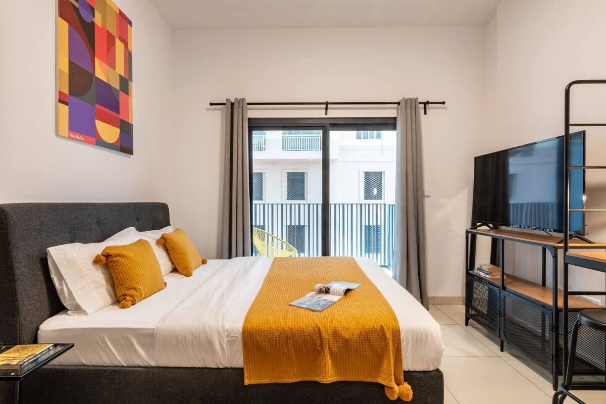A hotel room with a bed, a TV, a balcony, and a painting on the wall.