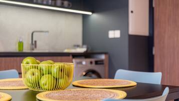 Una cocina moderna con una mesa de comedor preparada para cuatro personas, con individuales tejidos y un cuenco de manzanas verdes.