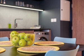 Une cuisine moderne avec une table à manger dressée pour quatre personnes, un saladier de pommes vertes et un lave-linge en arrière-plan.