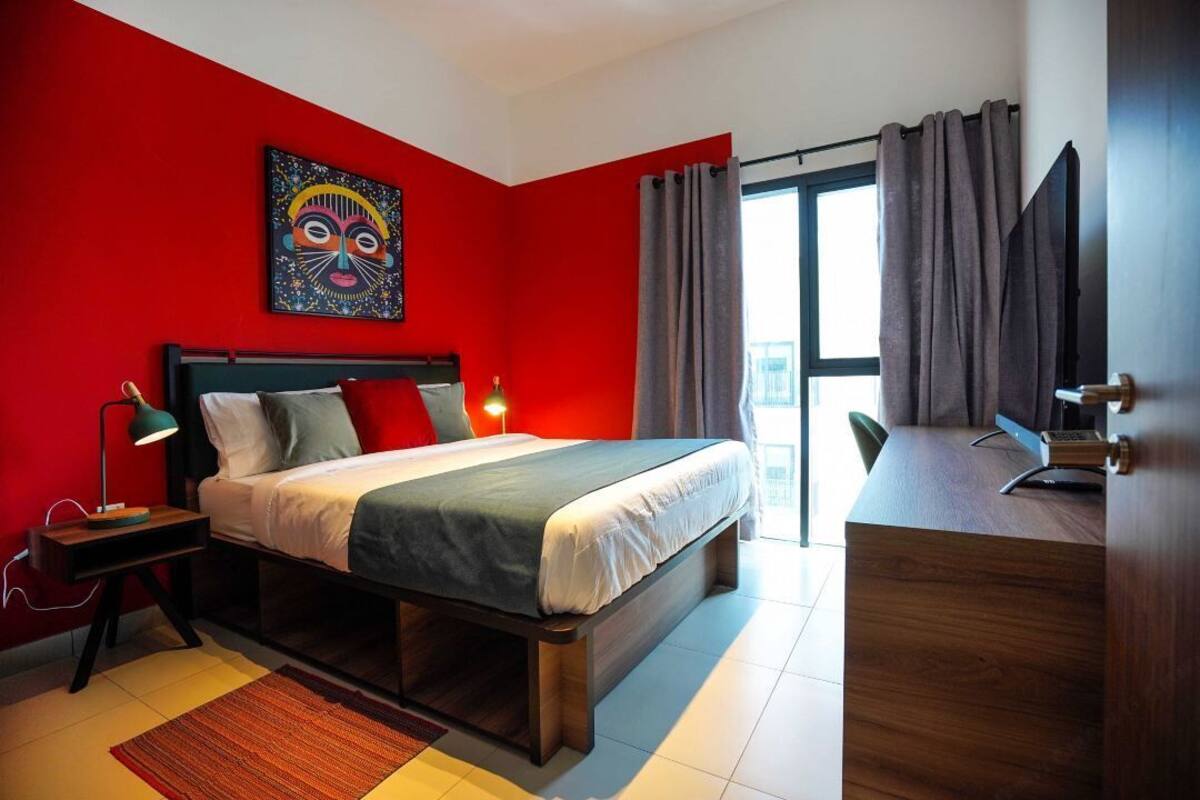 A modern hotel room with a large bed, a desk, and a red accent wall.