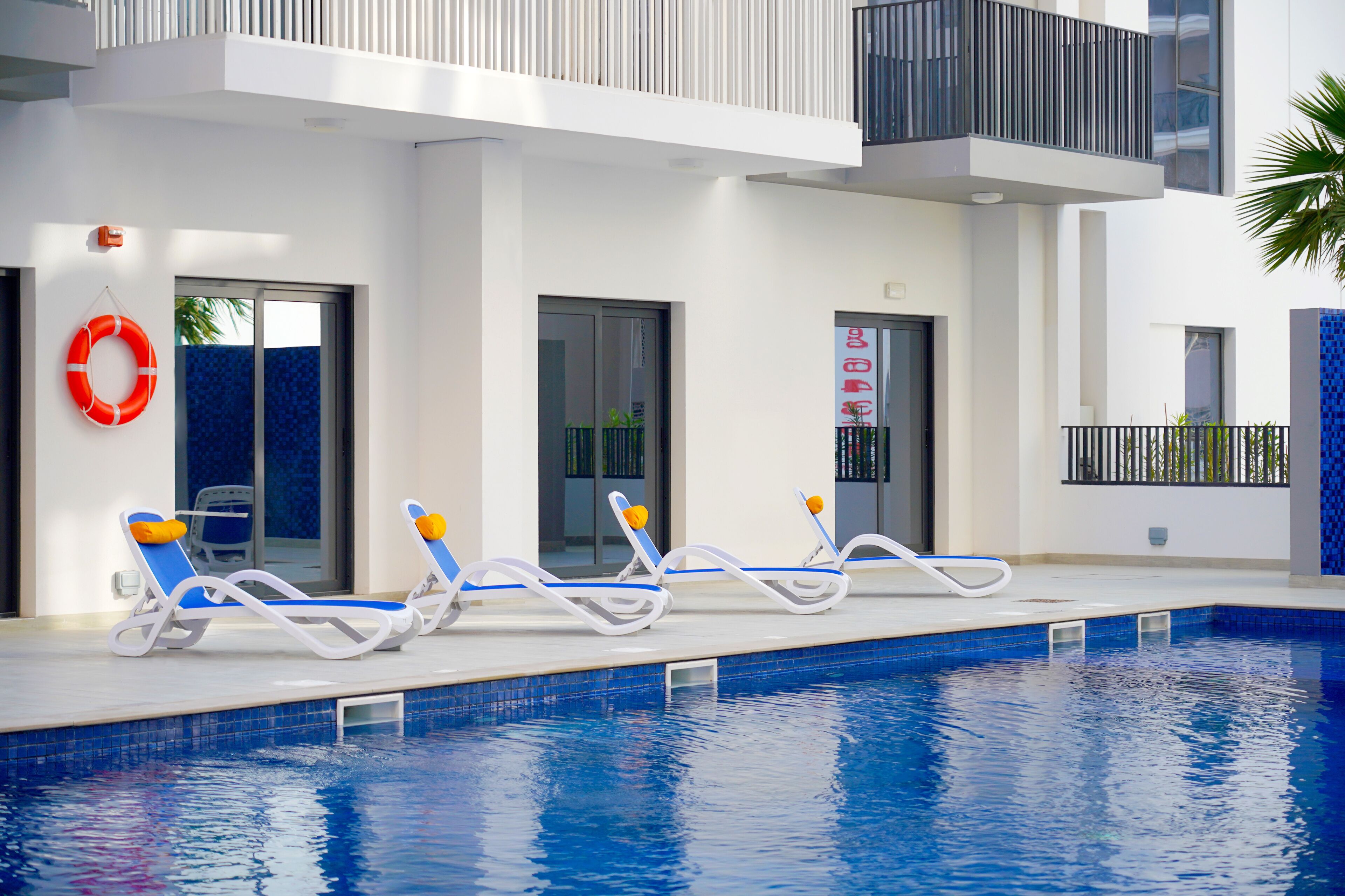 A swimming pool with lounge chairs and a lifebuoy, surrounded by a modern building with balconies.