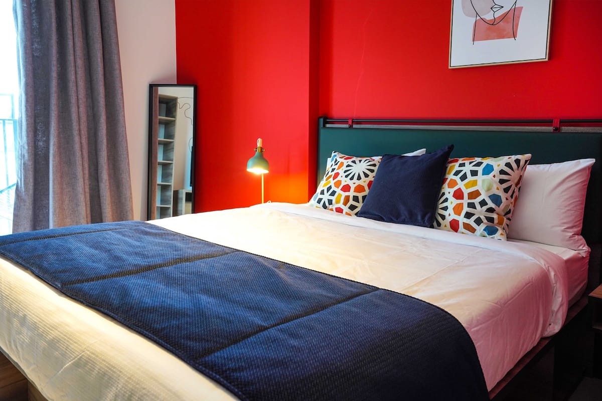A bed with a blue and white bedspread, a green headboard, and multiple pillows in various colors and patterns.