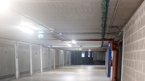 A clean, empty parking garage with concrete floors and walls, metal doors, and visible pipes and ducts. - SWEET HOME nice apartment near the marina (La Spezia)