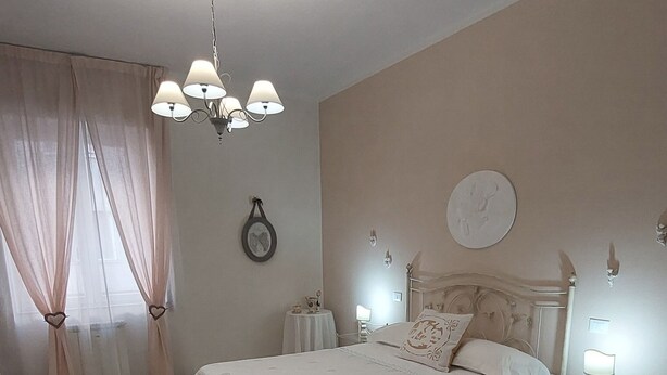 A bedroom with a bed, a chandelier, a bedside table, and a wall clock. - SWEET HOME nice apartment near the marina (La Spezia)