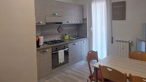A modern kitchen with a dining area. It includes a stove, sink, and cabinets. There is a dining table with chairs. - SWEET HOME nice apartment near the marina (La Spezia)