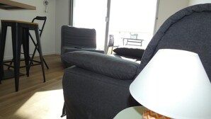 A modern living room with a grey sofa, a small table, and a lamp with a chevron pattern. - Seafront Studio at Notre-Dame-de-Monts 2 Pers (Notre-Dame-de-Monts)