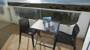 A balcony with a table and two chairs, overlooking a beach and the ocean. - Seafront Studio at Notre-Dame-de-Monts 2 Pers (Notre-Dame-de-Monts)