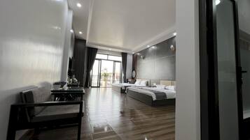 A modern hotel room with a large bed, a separate seating area with a table and chairs, and a balcony with a view.