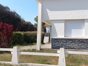 Un edificio moderno con base de piedra y paredes superiores blancas, una valla blanca en primer plano, y un cielo despejado.