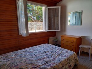 Un dormitorio con cama, cómoda, silla y ventana con vista a árboles.
