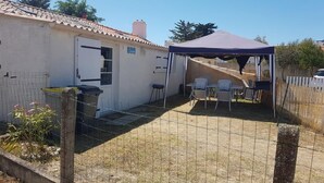 Un espace extérieur abrité avec une table et des chaises, un bâtiment blanc avec un toit en tuiles et une cour clôturée.