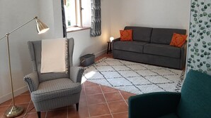A living room with a houndstooth armchair, a grey sofa with orange cushions, a floor lamp, and a patterned rug. - Golf getaway and relaxation at Domaine de Bisseret (Lavault-Sainte-Anne)