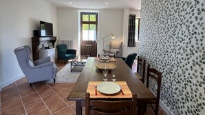 A dining area with a wooden table set for four, surrounded by chairs. A television is mounted on the wall, and there is a window with curtains. - Golf getaway and relaxation at Domaine de Bisseret (Lavault-Sainte-Anne)