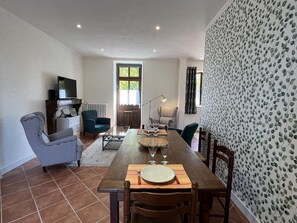 A dining area with a wooden table set for four, surrounded by chairs. A television is mounted on the wall, and there is a window with curtains. - Golf getaway and relaxation at Domaine de Bisseret (Lavault-Sainte-Anne)