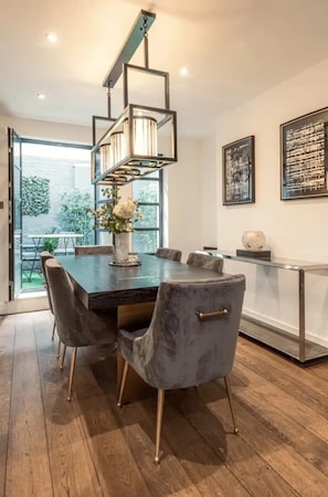 A modern dining area with a dark wooden table, grey upholstered chairs, and a hanging light fixture. - Luxurious & Central 3BD House - Chelsea (London)