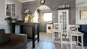 A modern kitchen with a built-in oven, a sink, and a dishwasher. There is a dining area with a table and chairs, and a living room with a sofa and a coffee table. - Canary Wharf two Bedroom Apartment (London)