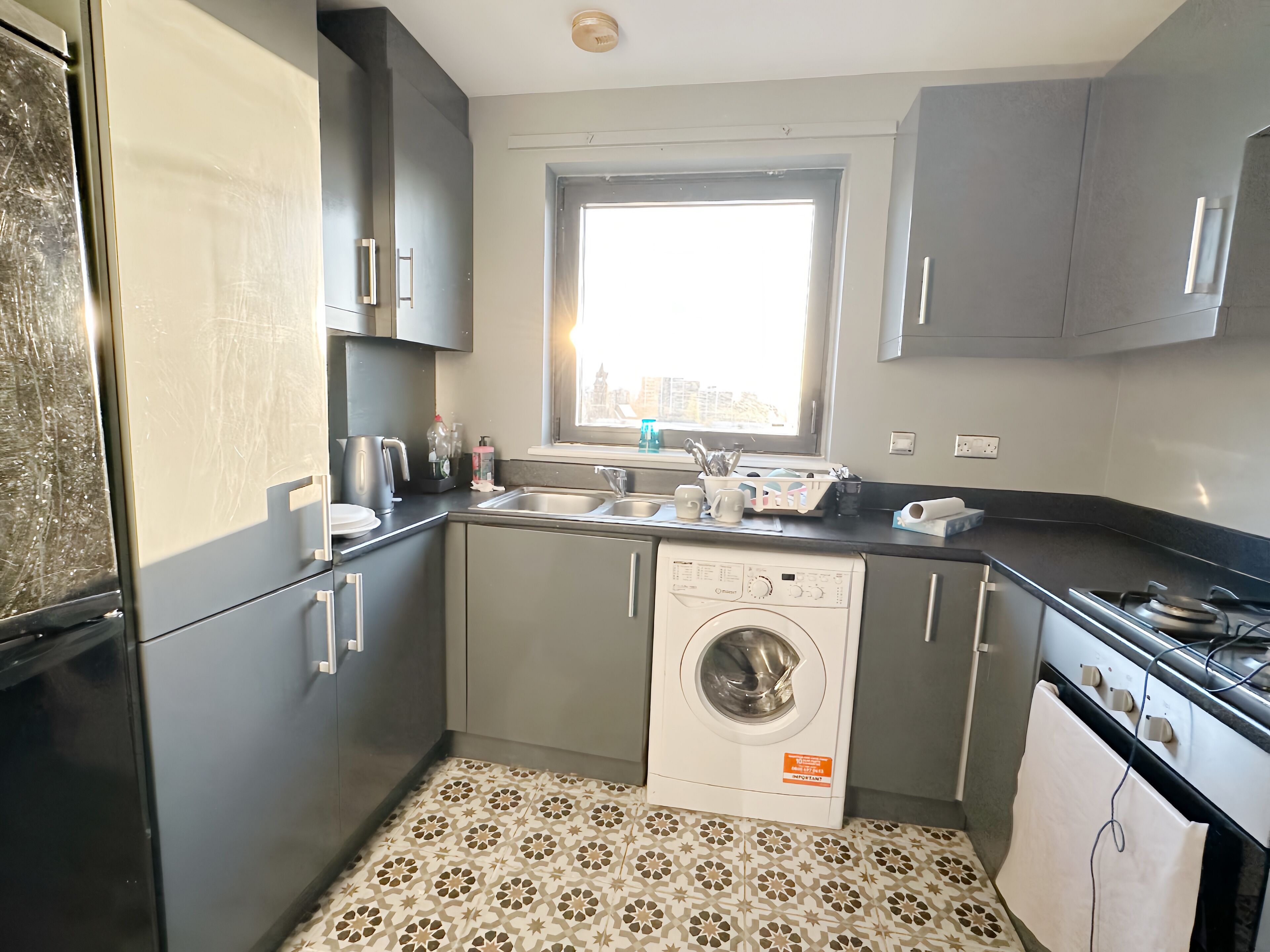A compact kitchen with a washing machine, a sink, and a window providing natural light.