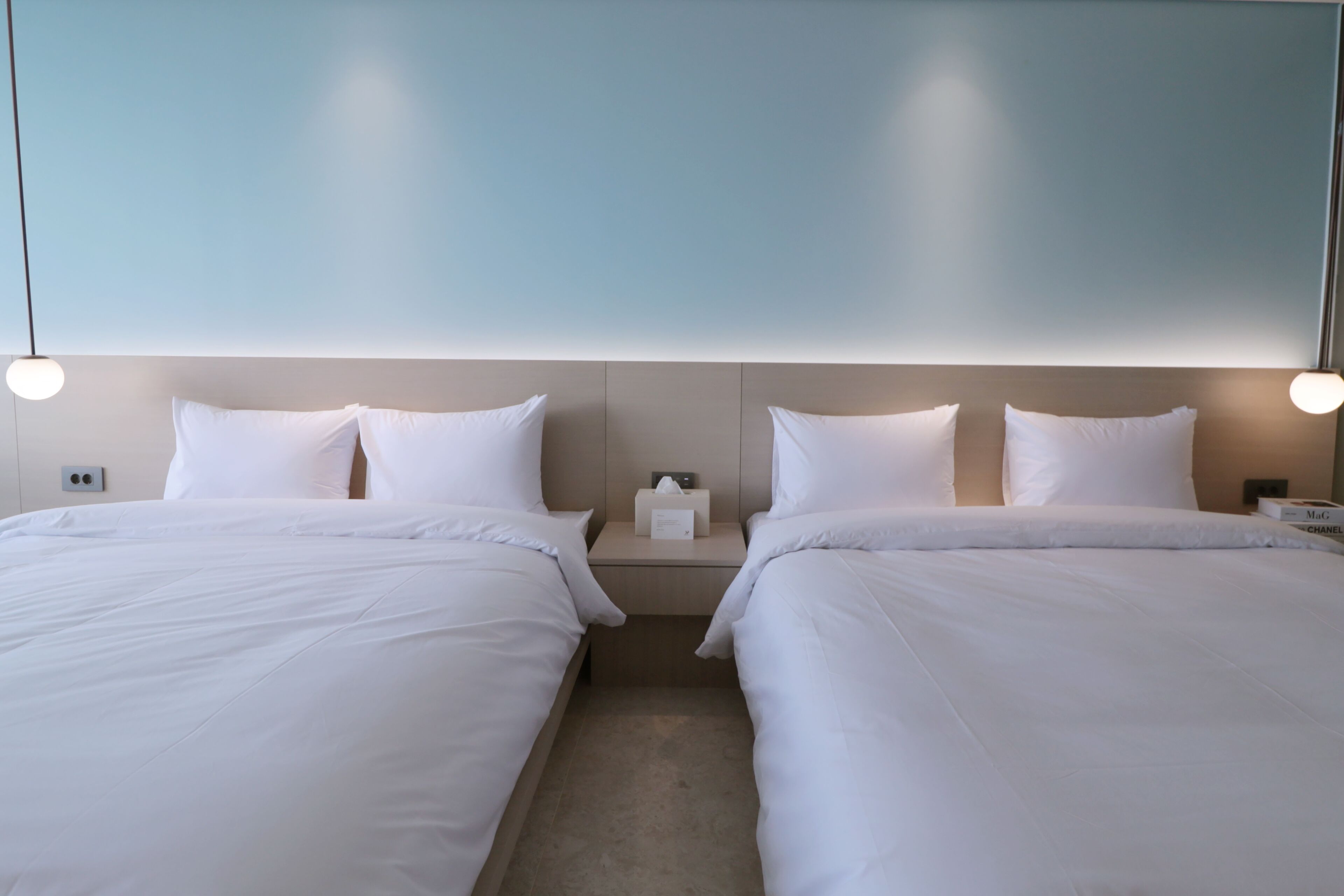 A hotel room with two beds, a nightstand with a lamp, and a wall-mounted light fixture.