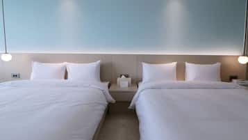 A hotel room with two beds, a nightstand with a lamp, and a wall-mounted light fixture.