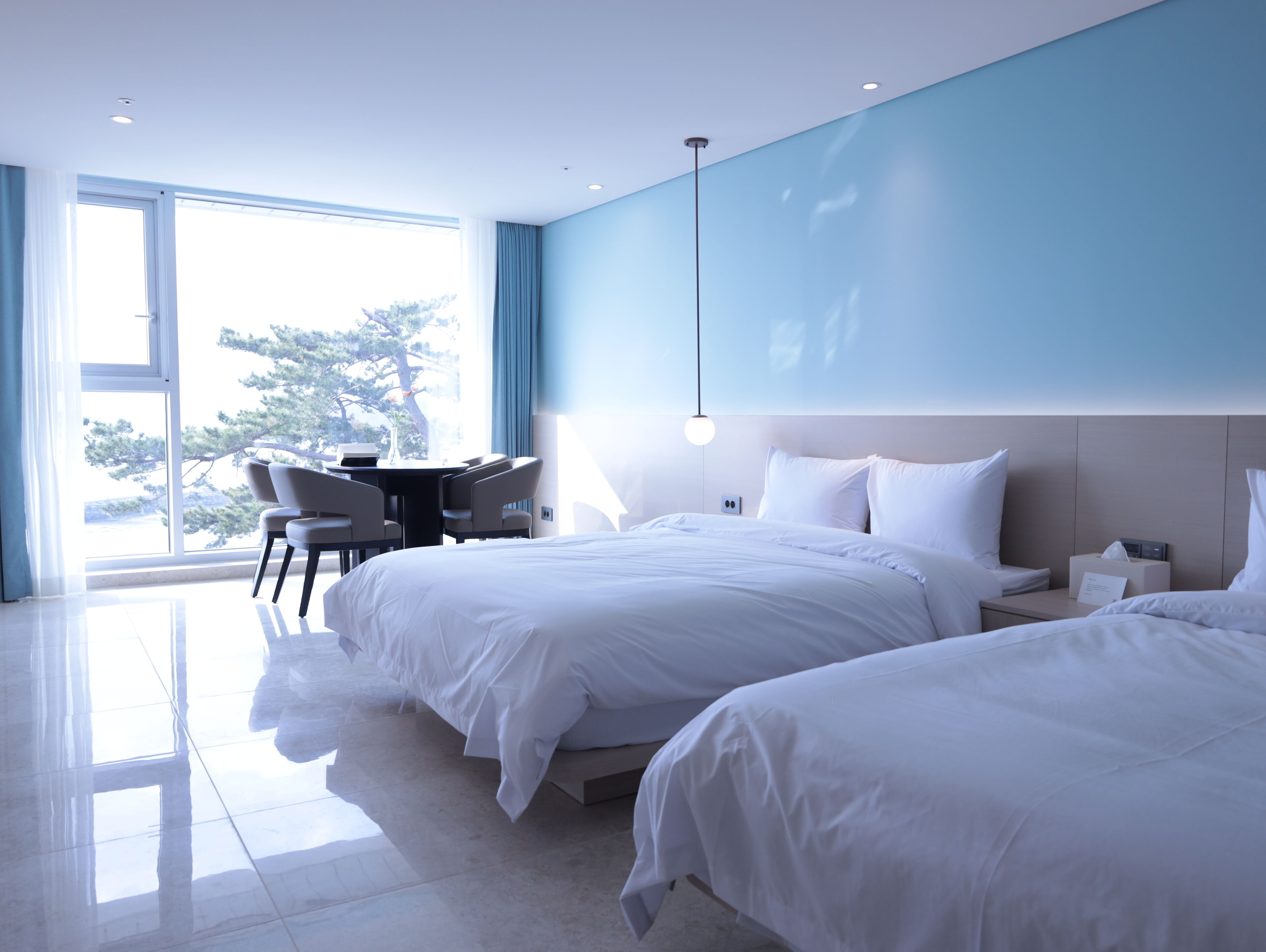 Quarto de hotel moderno com uma cama grande, uma escrivaninha e uma cadeira. Há uma janela com vista para árvores.