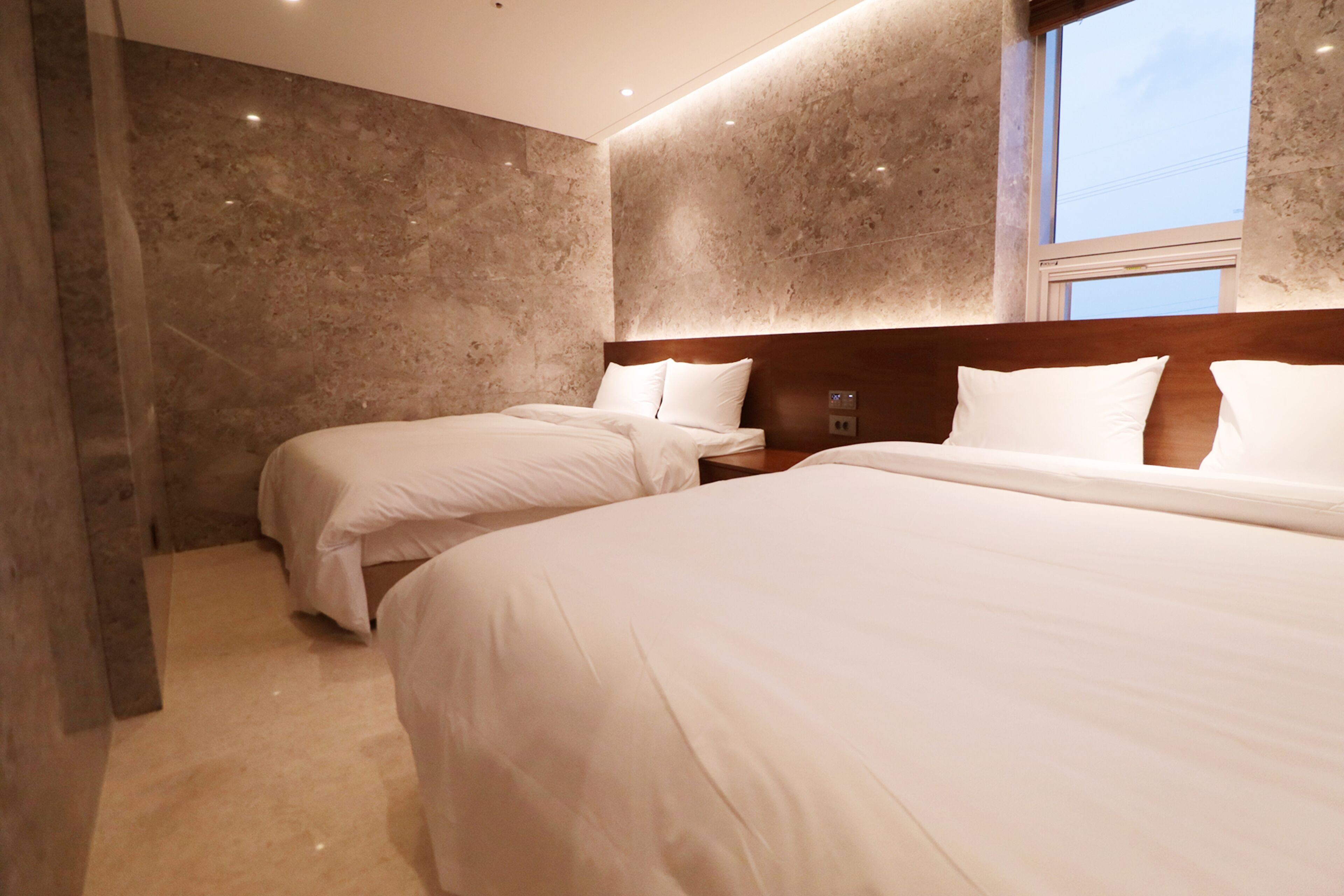 Een hotelkamer met twee bedden, marmeren wanden en een groot raam.