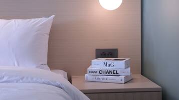 A neatly made bed with white linens, a wooden headboard, and a bedside table with a stack of books.