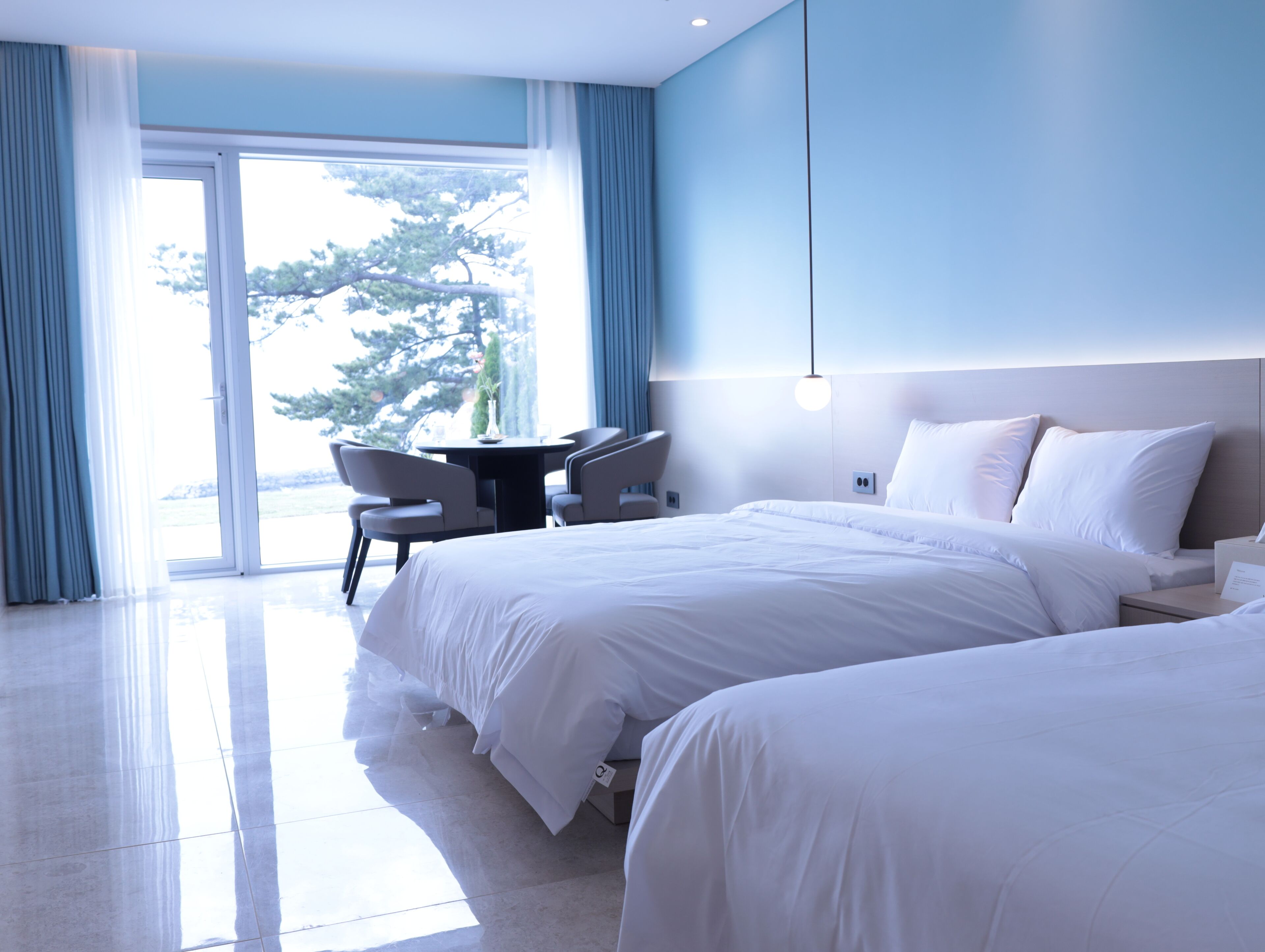 A hotel room with a large bed, a desk, and a chair. There is a window with curtains, and the room has a modern design.