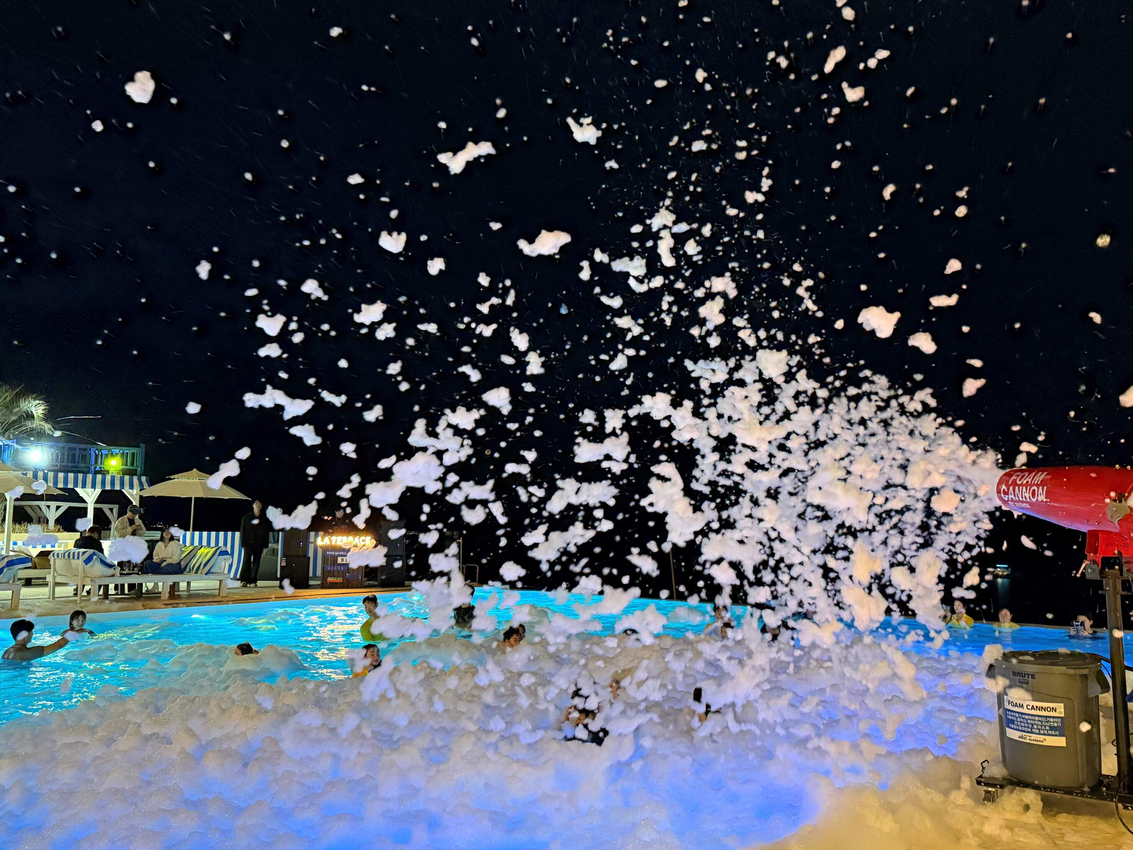 A pool area with people swimming and a foam cannon in operation.