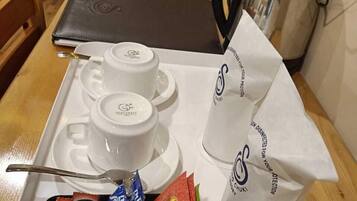 A tray with two white cups, a spoon, and a coffee pot. There are also packets of Nescafe and other coffee products.