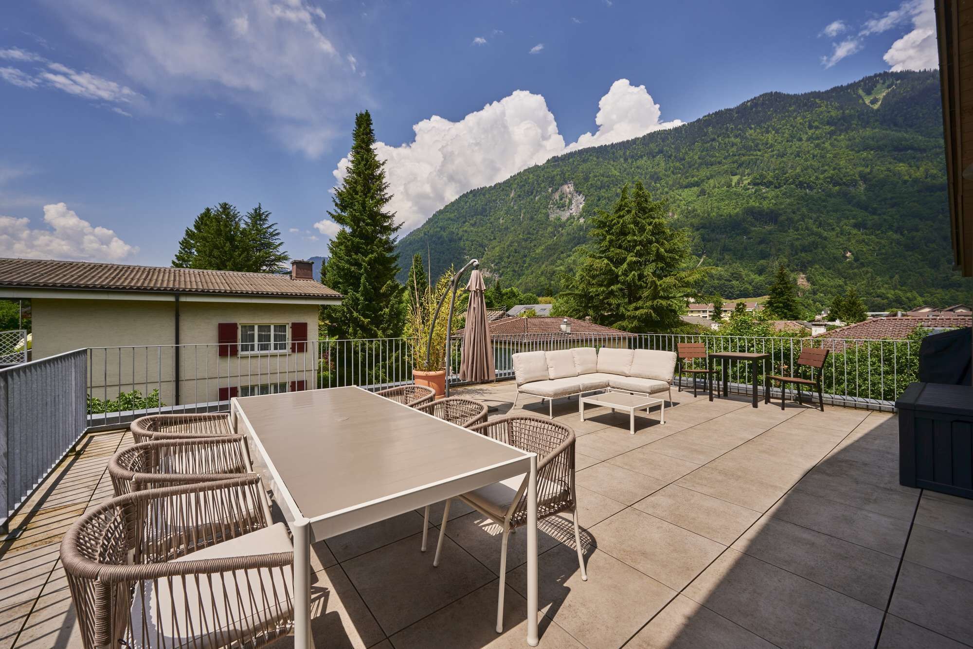 Une terrasse extérieure avec une table et des chaises, un canapé et une vue sur une montagne.