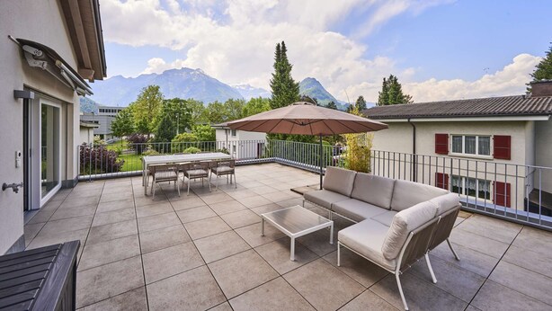 A balcony with a table, chairs, a sofa, and an umbrella.
