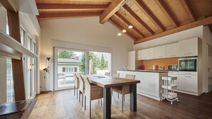 A modern kitchen with white cabinets, a wooden dining table, and a large window overlooking a garden.