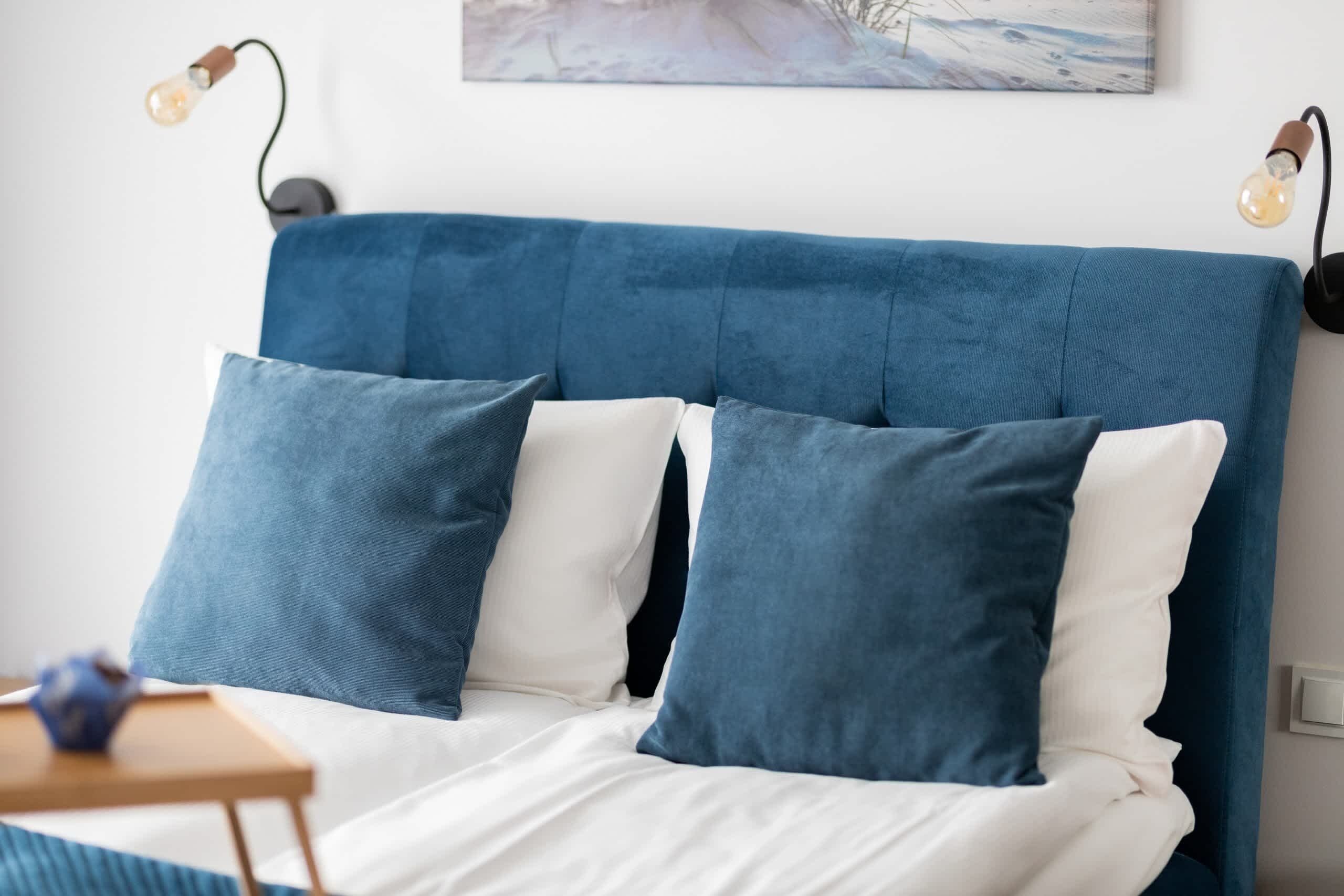 A bed with a blue headboard, white bedding, and two blue pillows.
