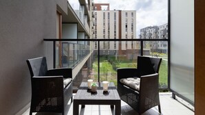 A balcony with wicker furniture and a table, overlooking a courtyard and buildings.