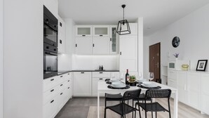 A modern kitchen with white cabinetry, a dining table with black chairs, and a hanging light fixture.