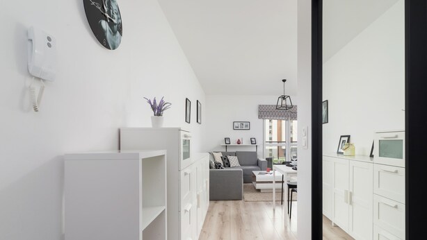 A modern, well-lit room with white cabinetry, a grey sofa, and a dining area with a white table and chairs.