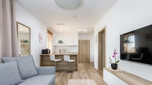 Una sala de estar moderna con un sofá gris, una mesa de centro con un jarrón rosa y un televisor montado en la pared.