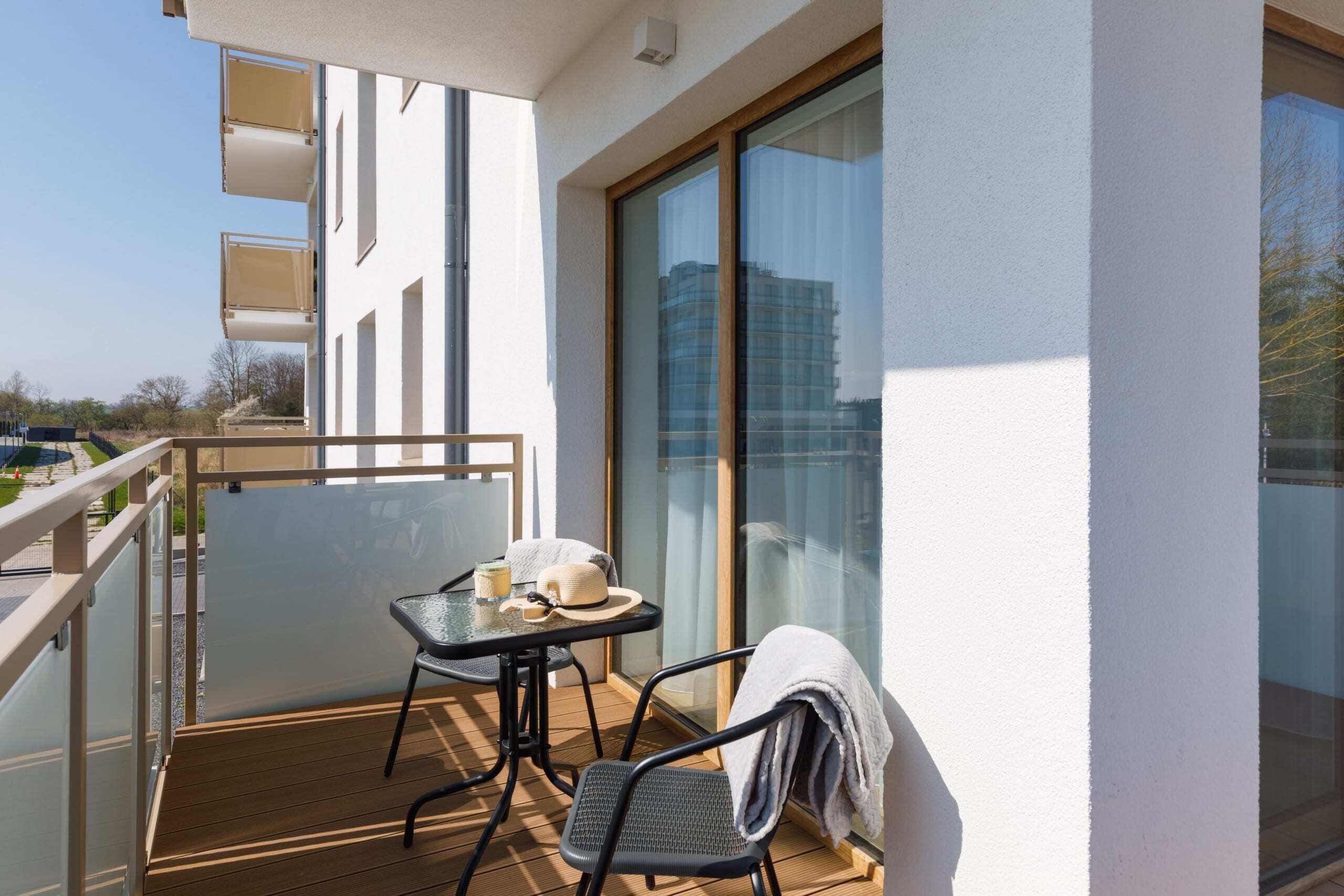 A balcony with a table and chairs, a view of the city, and a building with large windows.