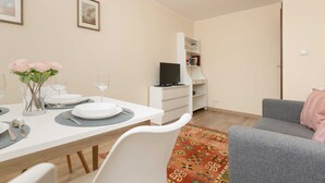 Un comedor con una mesa blanca dispuesta para cuatro personas, un sofá gris y una estantería al fondo.